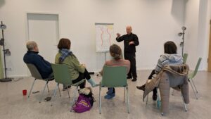 4 Personen hören sitzend einem Redner zu