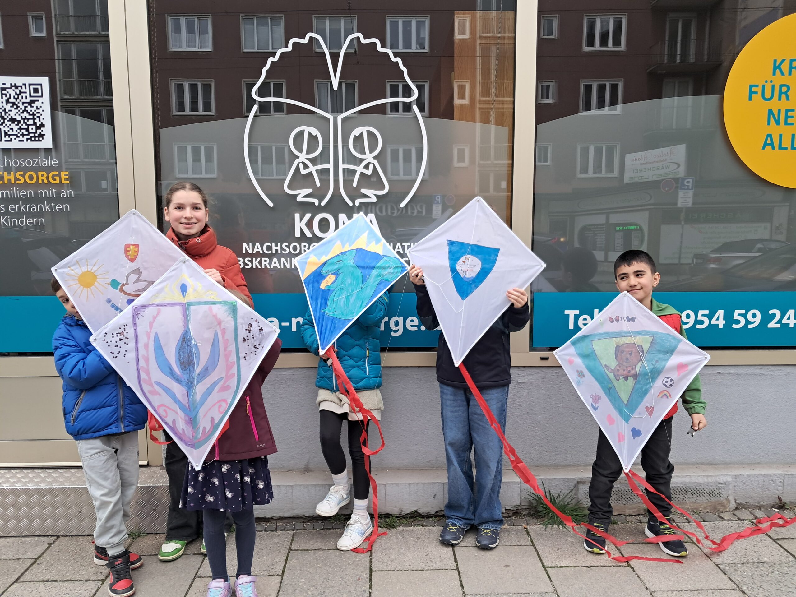 6 Kinder stehen vor dem Büro und halten selbstgebastelte Flugdrachen