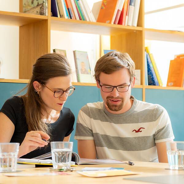 2 Personen sitzen am Tisch und betrachten ein Dokument