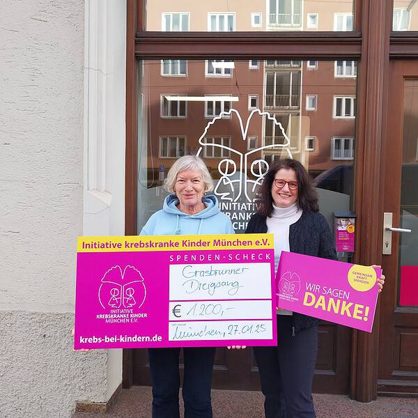 Zwei Frauen mit Spenden-Scheck vor der Tür der Initiative