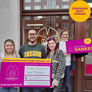 2Frauen und ein Mann halten einen Spendenscheck. Dahinter eine Frau mit Danke-Schild