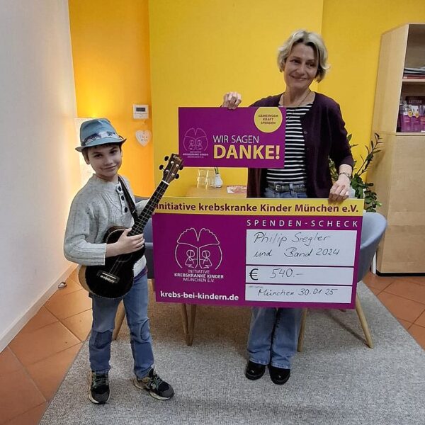 Bild eine Jungen mit Ukulele und einer Erwachsenen. Sie halten einen symbolischen Spendenscheck