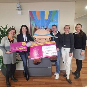 4 Frauen und ein Mann stehen um ein Plüschmaskottchen und zeigen den Spendenscheck