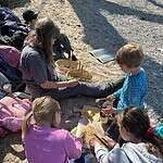 4 Kinder und eine Frau sitzen auf einer Sandbank und bereiten eine Brotzeit