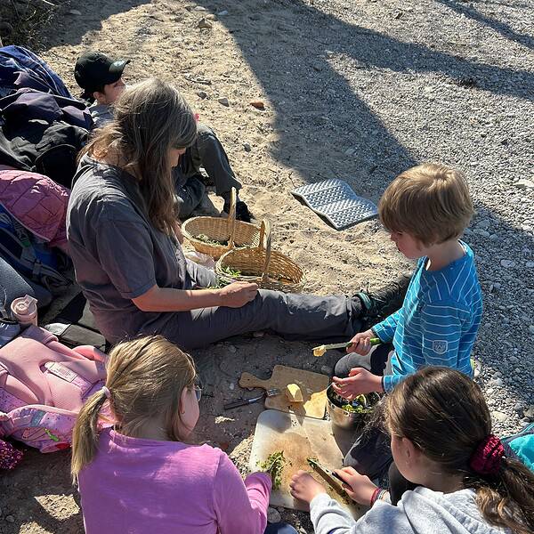 4 Kinder und eine Frau sitzen auf einer Sandbank und bereiten eine Brotzeit