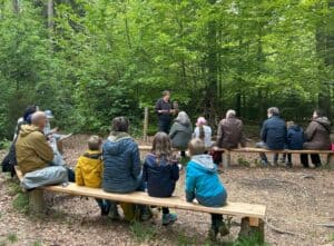 Familien sitzen im Wald vor einem Mann mit Eule auf dem Arm