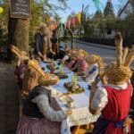 10 große Hasenfiguren sitzen an einem Langen Tisch neben einer Straße