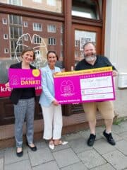 2 Frauen und ein Mann mit Spendenscheck vor der Ladentür