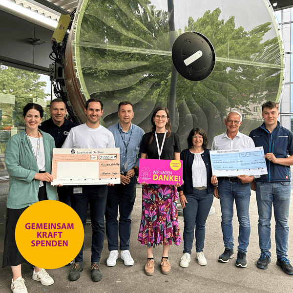 8 Personen mit 2 Spendenschecks vor großer Turbine