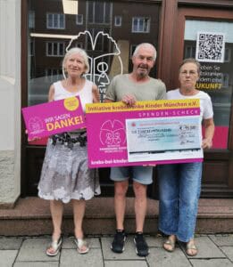 3 Personen mit Spendenscheck vor Ladenbüro