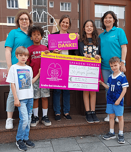 3 Frauen und 4 Kinder mit Spendenscheck vor dem Ladenbüro