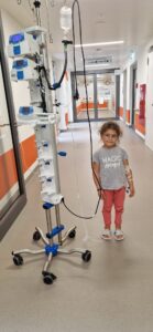 Kind steht auf Klinikflur mit Infusionsständer